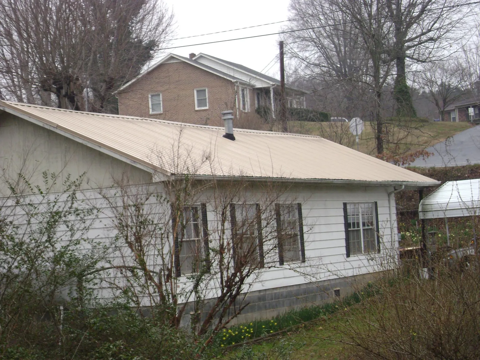 Tan metal roof on a white sided house set into a hillside — Commercial Roofing by Roofing Brothers in Frederick